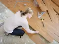 Frau kniet und verlegt Laminat. Werkzeuge wie Hammer und Winkel liegen bereit.