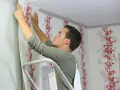 Mann tapeziert mit Vliestapete eine Wand mit rotem Blumenmuster.