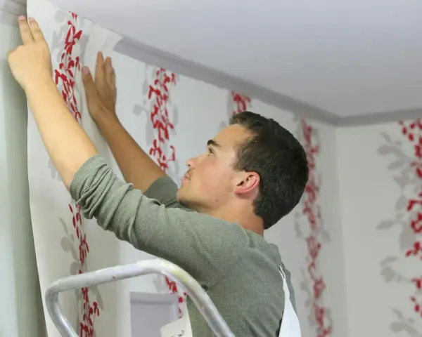 Mann tapeziert mit roter Blumenmuster-Tapete die Decke.