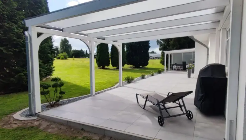 Moderne Terrasse bauen: Überdachter Sitzbereich mit Liegestuhl, Grill und Blick ins Grüne.
