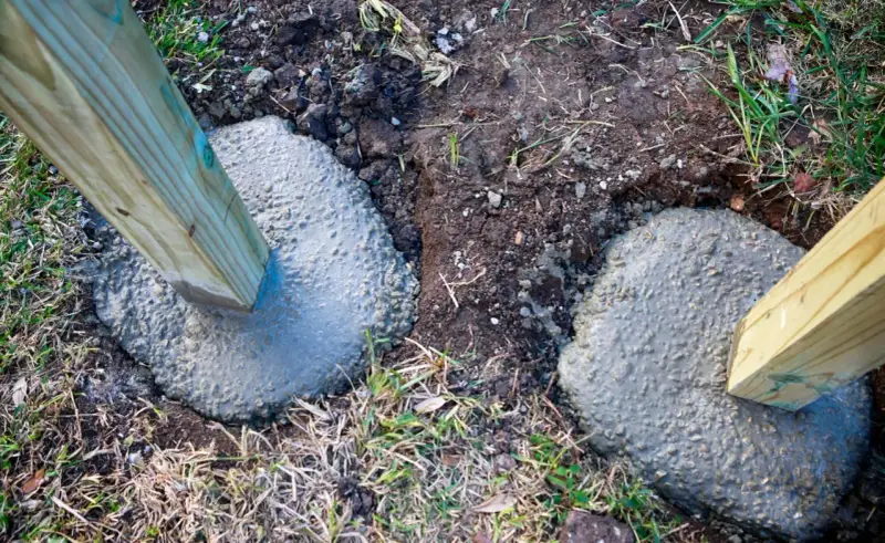 Holzpfosten werden in frisch gegossenen Beton gesetzt, um einen stabilen Zaun zu bauen. Das Einbetonieren der Zaunpfosten sorgt für Langlebigkeit.