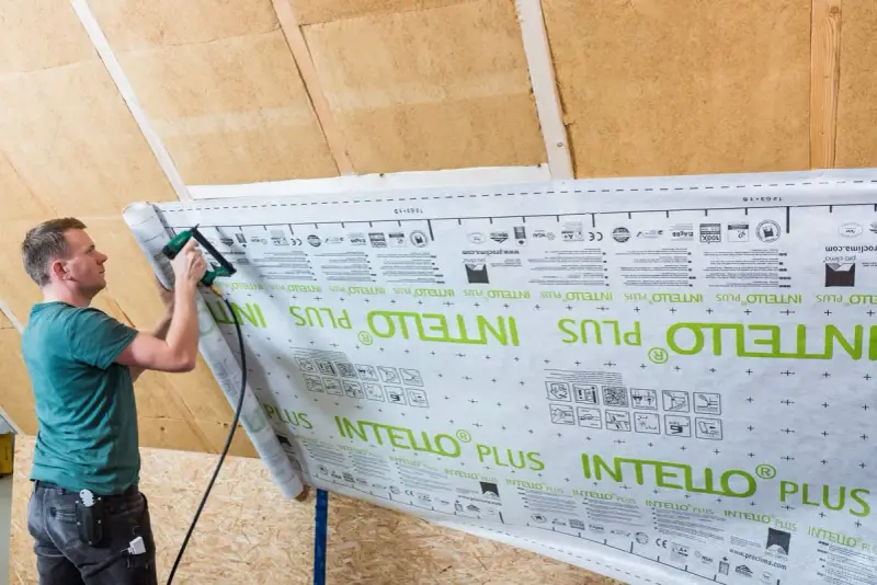 Mann bringt mit einem Tacker eine Dampfbremse an. Die Folie ist mit "INTELLO PLUS" bedruckt.
