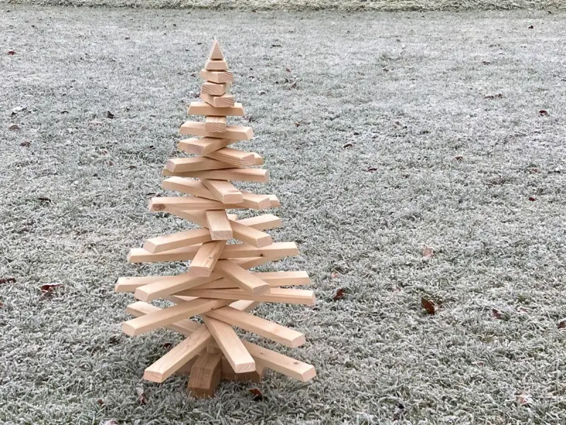 Ein selbstgemachter Tannenbaum aus Holz, der auf frostigem Gras steht. Eine rustikale Deko-Idee, um den Winter zu begrüßen.